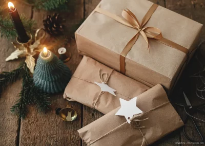 Verpackte Weihnachtsgeschenke liegen auf einem Tisch, während eine Kerze im Hintergrund brennt.
