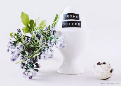 Ein Ei steht in einem Eierbecher. Auf dem Ei sind die Worte "Frohe Ostern" zu lesen.